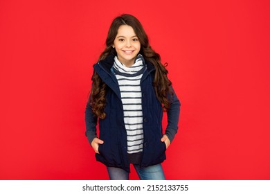 winter fashion. happy kid with curly hair in puffer waistcoat. teen girl on red background.
