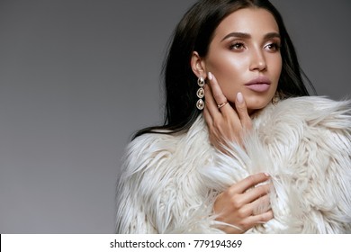 Winter Fashion Style. Beautiful Woman In Fur And Jewelry. Portrait Of Young Sexy Model With Beauty Makeup On Gorgeous Face In Luxury White Faux Fur Coat And Diamond Earrings. High Quality Image.