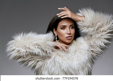 Winter Fashion Style. Beautiful Woman In Fur And Jewelry. Portrait Of Young Sexy Model With Beauty Makeup On Gorgeous Face In Luxury White Faux Fur Coat And Diamond Earrings. High Quality Image.