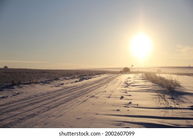 Winter fields on the background of the setting sun with trees in a vacant lot. Winter road on the background of trees. Winter sky