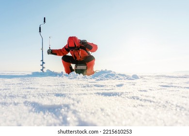 Winter fishing. A fisherman with a fishing rod tries to catch a fish in a frozen pond. Unrecognizable person. copy space - Powered by Shutterstock