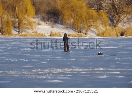 Winter fishing on the pond. Ice fishing. A fisherman stands and catches fish. Selective focus.