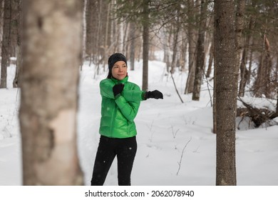 Winter Fitness Athlete Woman Warming Up Stretching Arms Before Her Outdoor Run Running On Snow Trail. Asian Runner Wearing Cold Weather Gloves, Headband, Jacket.