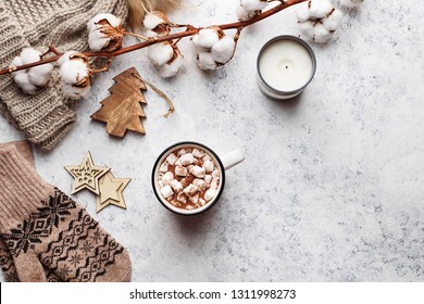 Winter Flat Lay With Mitten, Knitted Hat, Branch Of Cotton Flower, Candle And Mug With Hot Chocolate Or Cocoa With Marshmallow On Marble Background. Overhead View, Copy Space