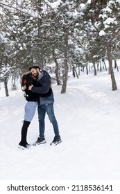 In the winter forest, winter holidays. A couple hugs and laughs on a background of a snowy forest.  young couple guy and a girl on snow. Giving valentines day red rose. Happy lover, love each other.