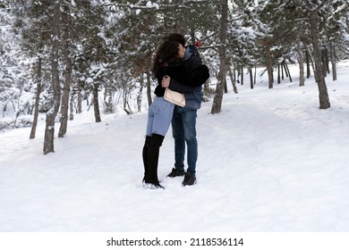 In the winter forest in love walks . winter holidays. A couple hugs and laughs on a background of a snowy forest.  young couple guy and a girl in a snowy forest. Giving valentines day red rose.