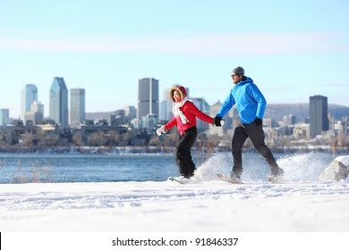 Winter Fun Couple On Snowshoes Running With Montreal Cityscape Skyline And River St. Lawrence In Background. Healthy Lifestyle Photo From Montreal, Quebec, Canada.