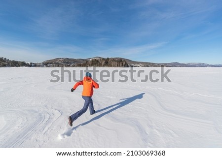 Winter fun in snow. Woman running on frozen lake in snowy winter nature landscape.