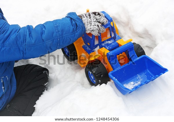Winter games Baby\
playing in the snow. Image of a child sitting on white snow and\
playing with a toy\
excavator.