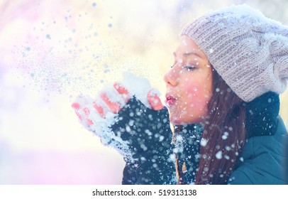 Winter Girl Blowing Snow. Beauty Joyful Teenage Model Girl Having Fun In Winter Park. Beautiful Young Woman Laughing Outdoors. Enjoying Nature.