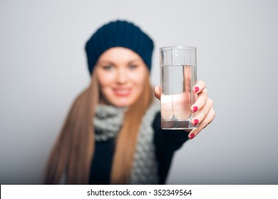 Winter girl gives to drink a glass of water. Lifestyle studio photo isolated portrait of a woman on a gray background.