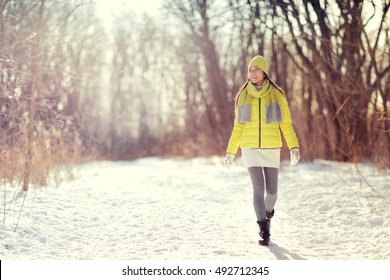 Winter Happy Woman Walking In Snow Outdoors Nature. Joyful Young Person Relaxing On An Outdoor Walk Activity In Snowy Forest Landscape Wearing Warm Yellow Fashion Outerwear Jacket Boots, Scarf, Hat.