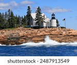 Winter Harbor Lighthouse with dramatic waves of Atlantic Ocean on the foreground, Maine, USA 