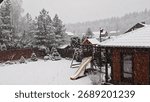 Winter has returned in the middle of spring. Heavy snow is falling with large snowflakes. Snow lies on the grassy lawn, playground, on the trees and on the roof of a wooden house