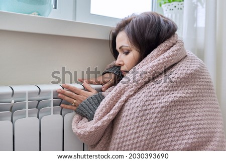 Winter, heating season. Woman in warm sweater sitting in home room near heating radiator