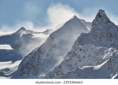 Winter high mountain landscape covered in clouds and snow, jagged rock ridge formations, snowing