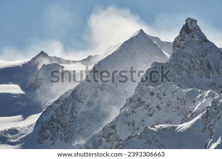 Winter high mountain landscape covered in clouds and snow, jagged rock ridge formations, snowing