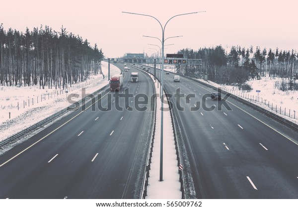 Winter highway with trucks and cars\
among winter forest. Vintage style retro toned\
picture.