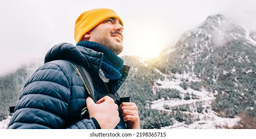 Winter hike on snow mountain young happy hiker man climbing. Europe travel adventure trek in nature landscape. Young cheerful person wearing yellow hat, blue jacket for cold weather and bag. - Shutterstock ID 2198365715