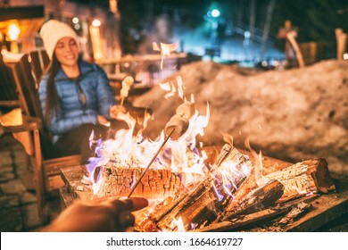 Winter holiday ski resort woman roasting marshmallows in BBQ firepit afterski fun leisure activity with friends. Couple grilling marshmallow stick in fire.
