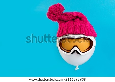 Winter holidays. A balloon floating on a blue background wearing a ski mask and a winter hat. Concept of tourism and winter sports