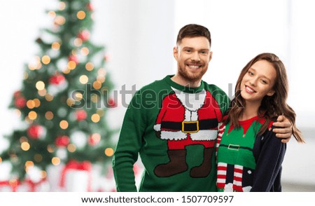 winter holidays, celebration and people concept - portrait of happy couple in ugly sweaters at home over christmas tree lights background