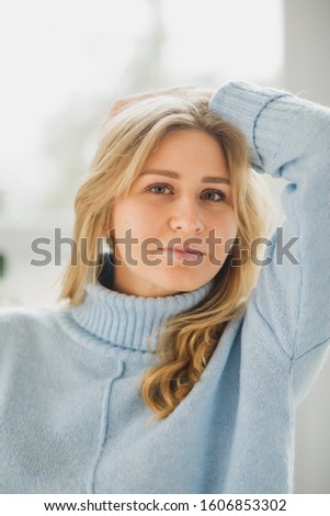winter holidays, celebration and people concept - happy young woman wearing blue sweater with reindeer pattern over festive christmas tree lights background