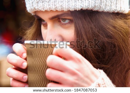 Winter holidays, christmas, hot drinks and people concept. Close up portrait of beautiful young woman tourist in warm clothes drinking coffee from disposable paper cups in old town
