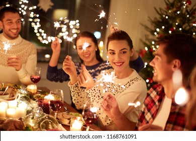 winter holidays and people concept - happy friends with sparklers celebrating christmas at home feast