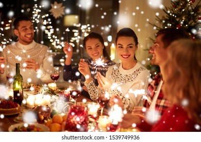 winter holidays and people concept - happy friends with sparklers celebrating christmas at home feast over snow