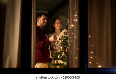 winter holidays and people concept - happy couple decorating christmas tree at home - Powered by Shutterstock