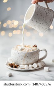 Winter Hot Drink. Hot Chocolate Or Cocoa With Marshmallow And Spices On White Background With Bokeh Lights. Hand Pouring Milk