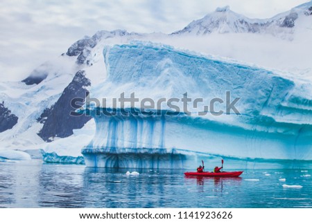 winter kayaking in Antarctica, extreme sport adventure, people paddling on kayak near iceberg