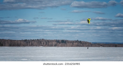 Winter Kitesurfing in solo with yellow kite in the Quebec Laurentian region on a slightly cloudy winter day 