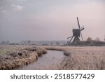 Winter landscape with a Dutch windmill on the edge of a river in the early morning at sunrise when all nature is frozen like in a fairy tale