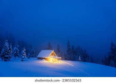 A winter landscape featuring an isolated wooden cabin and snow-covered fir trees on a mountain meadow deep within the forest. Christmas postcard. Snowy mountains forest - Powered by Shutterstock