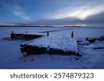 Winter landscape featuring a snow-covered dock by a frozen lake at dusk