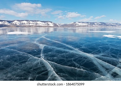 Winter landscape of frozen lake Baikal on a sunny February day. Beautiful blue smooth ice with cracks in the Small Sea Strait. Ice travel in winter holidays. Natural background (focus on ice) 