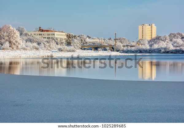 Winter landscape - the\
ice on the river and the building on its shore, which are reflected\
in the water.