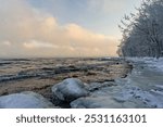 Winter landscape of Karelia: icy shore of Lake Ladoga, snow-covered forest, fog over the water, changing into light clouds