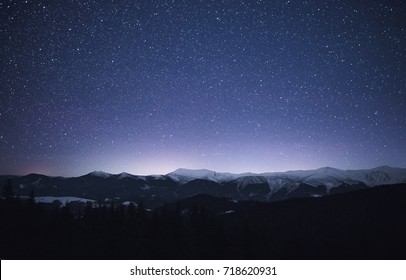 Winter Landscape Of A Mountain Range At Night. Stars Over The Mountain Range. Snow Covers Slopes Of A Mountains.