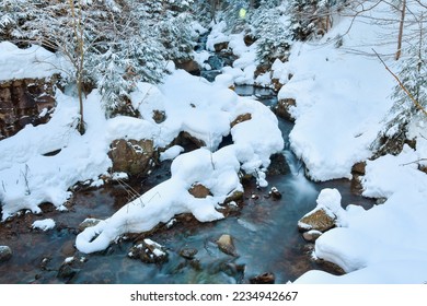 Winter landscape of a mountain river, the water slowly flows down the river bed between snow-covered stones.
