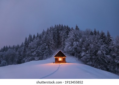 Winter Landscape. Mystical Night. Old Wooden Hut On The Lawn Covered With Snow. The Lamps Light Up The House At The Evening Time. Mountains And Forests. Wallpaper Background.