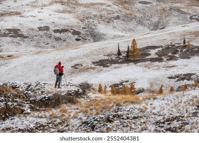 Winter landscape photographer with backpack explores snowy Altai Mountains landscape, surrounded by rugged terrain and sparse trees, capturing nature's beauty. - Powered by Shutterstock