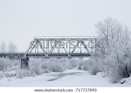 Winter landscape with railroad bridge over frozen river, snow-covered trees, hoarfrost.