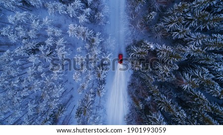 Winter landscape with red car driving at night. Lights of car and winter snowy road in dark forest, big fir trees covered snow. Top down view. 