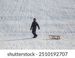 Winter landscape in Riem park, Munich, Bavaria, Germany: Boy with his sled on his way up the hill for the next sled ride