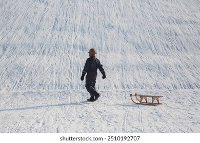 Winter landscape in Riem park, Munich, Bavaria, Germany: Boy with his sled on his way up the hill for the next sled ride