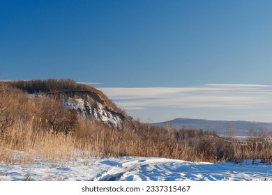 Winter landscape. Road covered with snow and a hill with tall dry grass on a sunny day. - Powered by Shutterstock