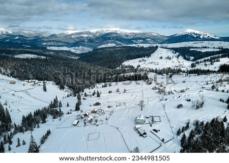Winter landscape with small village houses between snow covered forest in cold mountains